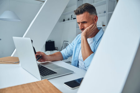 Tired mature man working on laptop while sitting at the office desk
