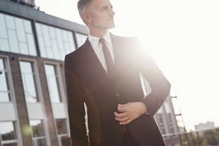 Confident mature businessman walking near office building outdoorsの写真素材