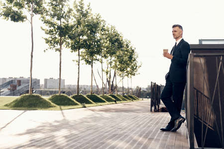 Full length of confident mature businessman holding coffee cup while standing outdoorsの写真素材