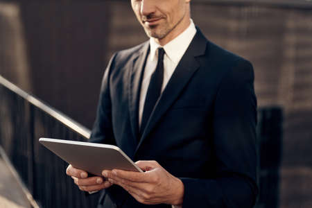 Close up of confident mature businessman working on digital tablet while standing outdoorsの写真素材
