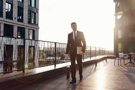 Confident mature man in full suit carrying laptop while walking by business center terrace outdoorsの写真素材
