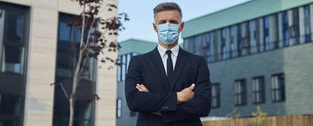 Confident mature businessman in protective face mask looking at camera while standing outdoorsの写真素材
