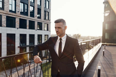 Confident mature man in full suit standing on business center terraceの写真素材