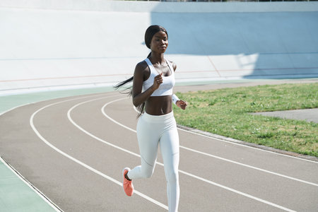 Confident young African woman in sports clothing running on track outdoors