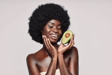 Portrait of beautiful young African woman holding avocado and smiling