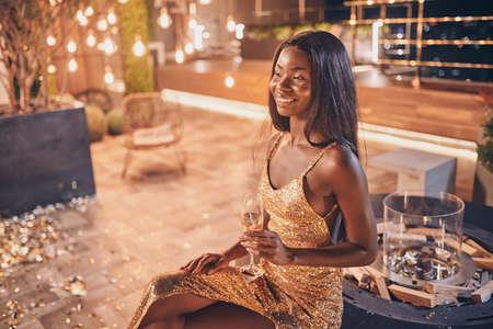 Beautiful young African woman in evening gown holding flute with champagne and smilingの写真素材
