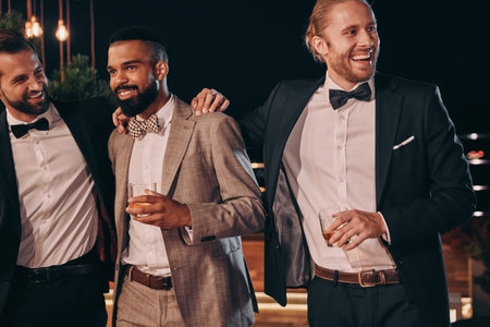 Three handsome men in suits bonding and drinking whiskey while spending time on party