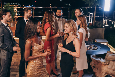 Group of beautiful young people in formalwear communicating and smiling while spending time on...