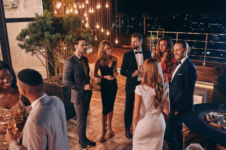 Group of people in formalwear communicating and smiling while spending time on luxury party
