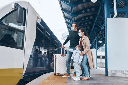 Full length of family with two little kids wearing protective face masks and standing on railroad station platformの写真素材