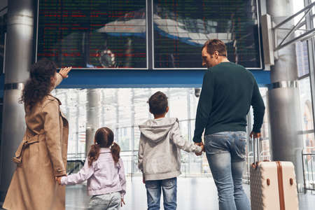 Rear view of family with two little kids looking at the flight information boardの写真素材