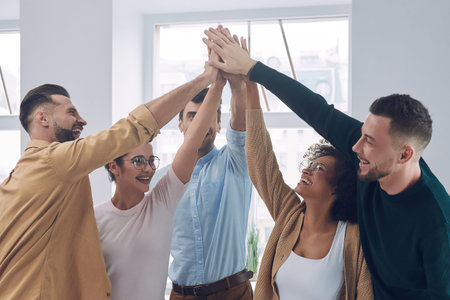 Group of happy young people in smart casual wear holding hands together and smiling while having...