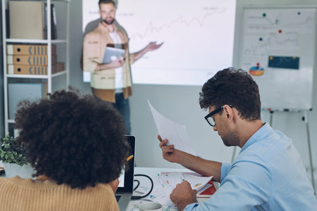 Group of young modern people in smart casual wear analyzing data on projection screen in the office