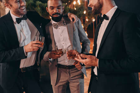 Three well-dressed men drinking whiskey and communicating while spending time on partyの写真素材