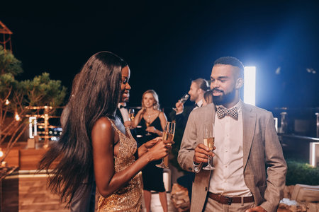 Beautiful young couple in formalwear holding champagne flutes and smiling while spending time on...