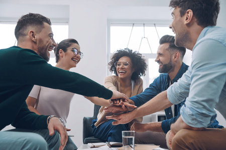 Confident young business team keeping hands clasped and smiling while sitting in the office together