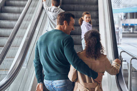 Happy family with two little kids moving by escalator in airport terminalの写真素材