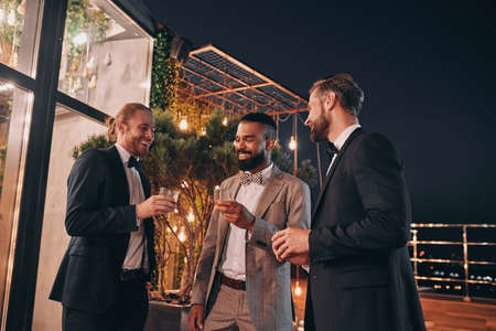 Three handsome men in suits drinking whiskey and communicating while spending time on partyの写真素材