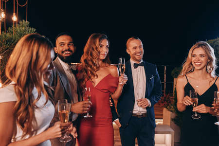 Group of beautiful people in formalwear communicating and smiling while spending time on luxury partyの写真素材