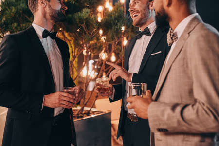 Close-up of three well-dressed men drinking whiskey and communicating while spending time on partyの写真素材