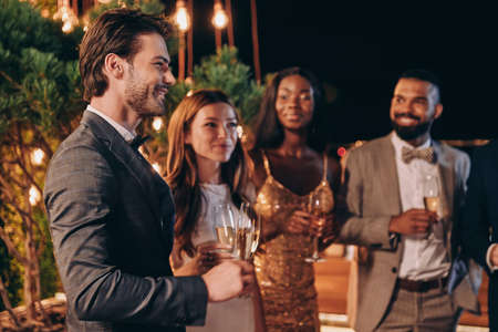 Group of beautiful young people in formalwear communicating and smiling while spending time on luxury partyの写真素材