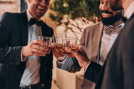 Close-up of three well-dressed men drinking whiskey and communicating while spending time on partyの写真素材