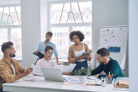 Group of confident young people in smart casual wear discussing business while having meeting in officeの写真素材