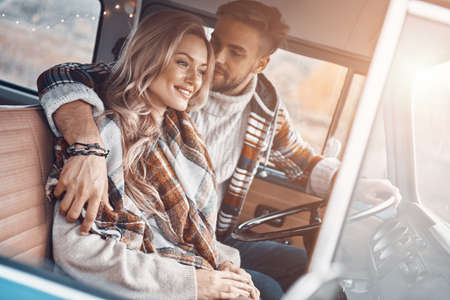 Beautiful young loving couple enjoying road trip together while sitting on front seats of retro mini vanの写真素材