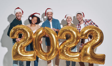 Group of young beautiful people in Christmas hats carrying gold colored numbers and smiling