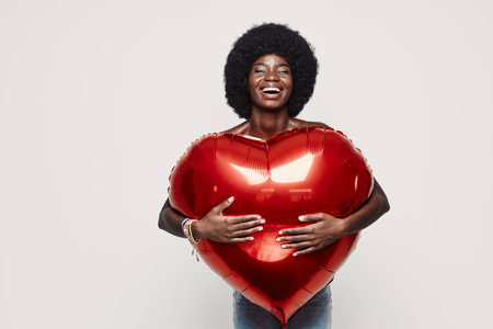Beautiful young African woman holding red heart shape balloon and smilingの写真素材