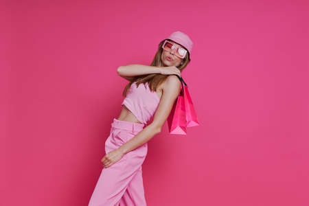 Playful young woman carrying shopping bags while standing against pink backgroundの写真素材