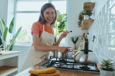 Beautiful young woman tasting soup while cooking at the domestic kitchen