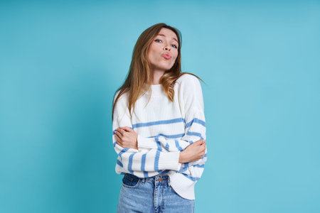Attractive young woman sending a kiss while standing against blue background