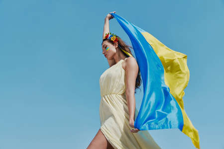 Attractive Ukrainian woman carrying national flag with sky in the backgroundの写真素材