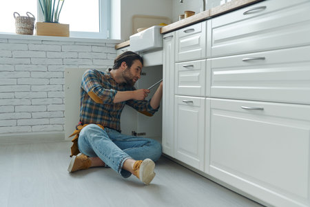 Confident young handyman fixing a sink at the domestic kitchen