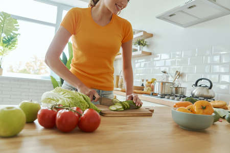 Close-up of young woman cutting vegetables at the domestic kitchenの写真素材