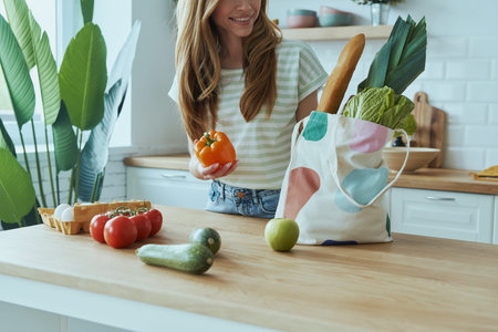 Close-up of young woman unpacking the bag with healthy food while standing at the domestic kitchen