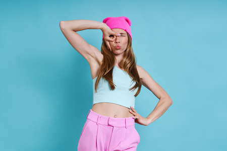 Playful young woman in pink hat having fun against blue backgroundの写真素材