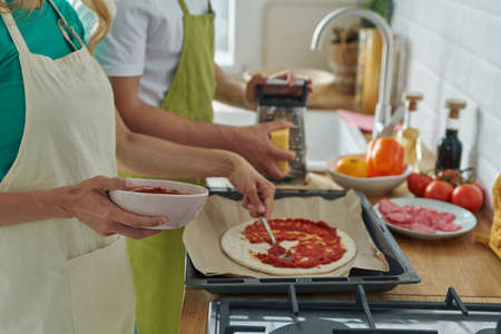 Close-up of couple making homemade pizza while standing at the kitchen togetherの写真素材