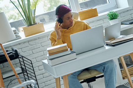Confident mixed race man in headphones using laptop while working in office