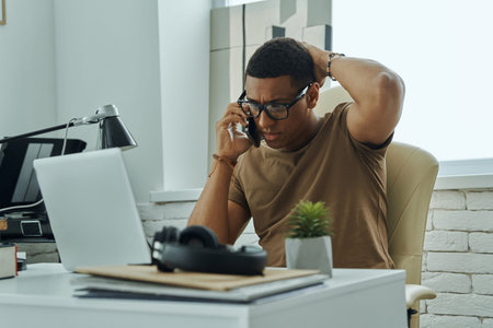 Worried young mixed race man talking on mobile phone while working in office