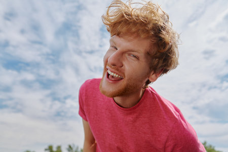 Handsome young redhead man looking at camera and smiling with sky in the backgroundの写真素材
