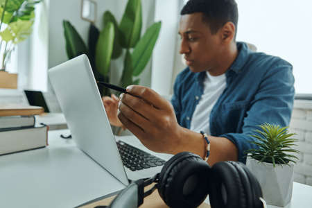 Concentrated young mixed race man using laptop while working in the officeの写真素材