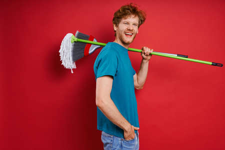 Handsome young man carrying cleaning equipment on shoulder while against red backgroundの写真素材