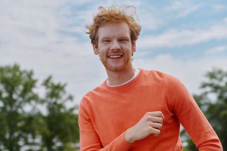 Cheerful young redhead man looking at camera and smiling while standing outdoorsの写真素材