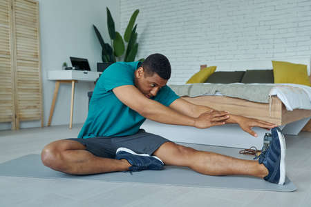 Confident young multiracial man in sports clothing exercising at homeの写真素材