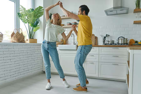 Full length of beautiful young couple dancing at the domestic kitchenの写真素材