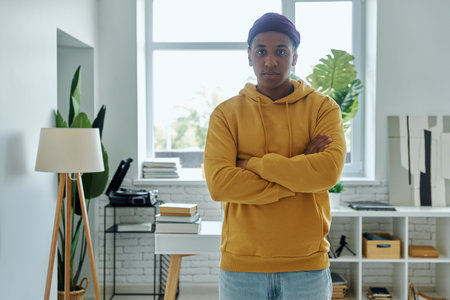 Handsome multiracial man keeping arms crossed while standing at home office