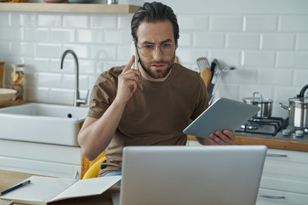 Concentrated man talking on mobile phone and using technologies while working from home