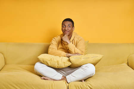 Thoughtful mixed race man relaxing on the couch with yellow backgroundの写真素材